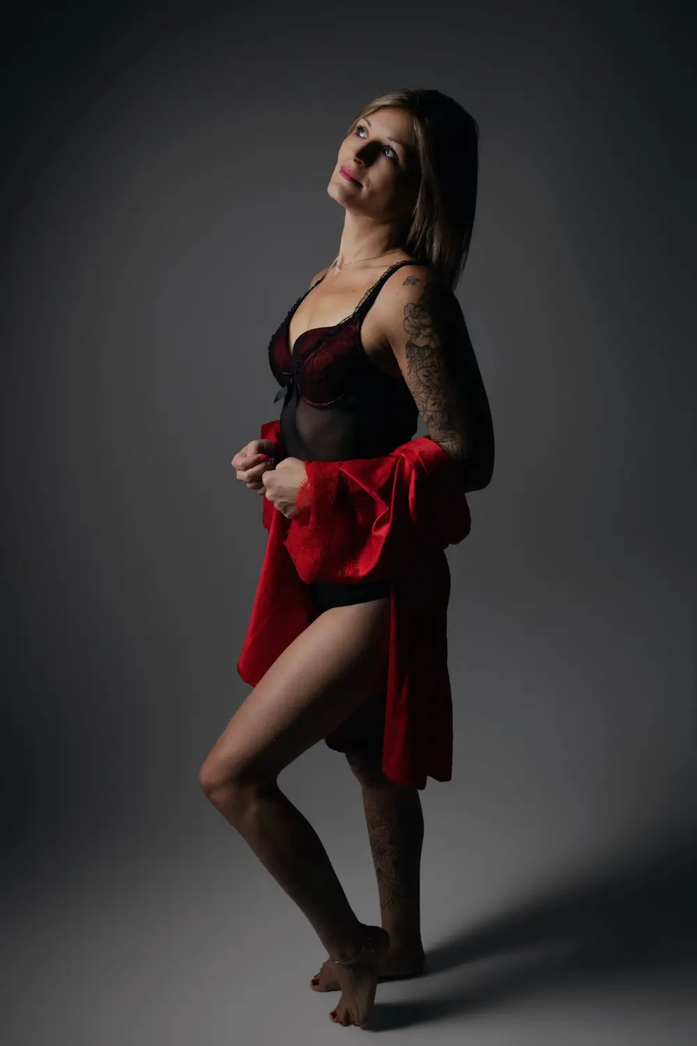Femme tatouée en lingerie noire et peignoir rouge, debout dans un clair-obscur de studio, portrait boudoir - Cindy Poulet photographe